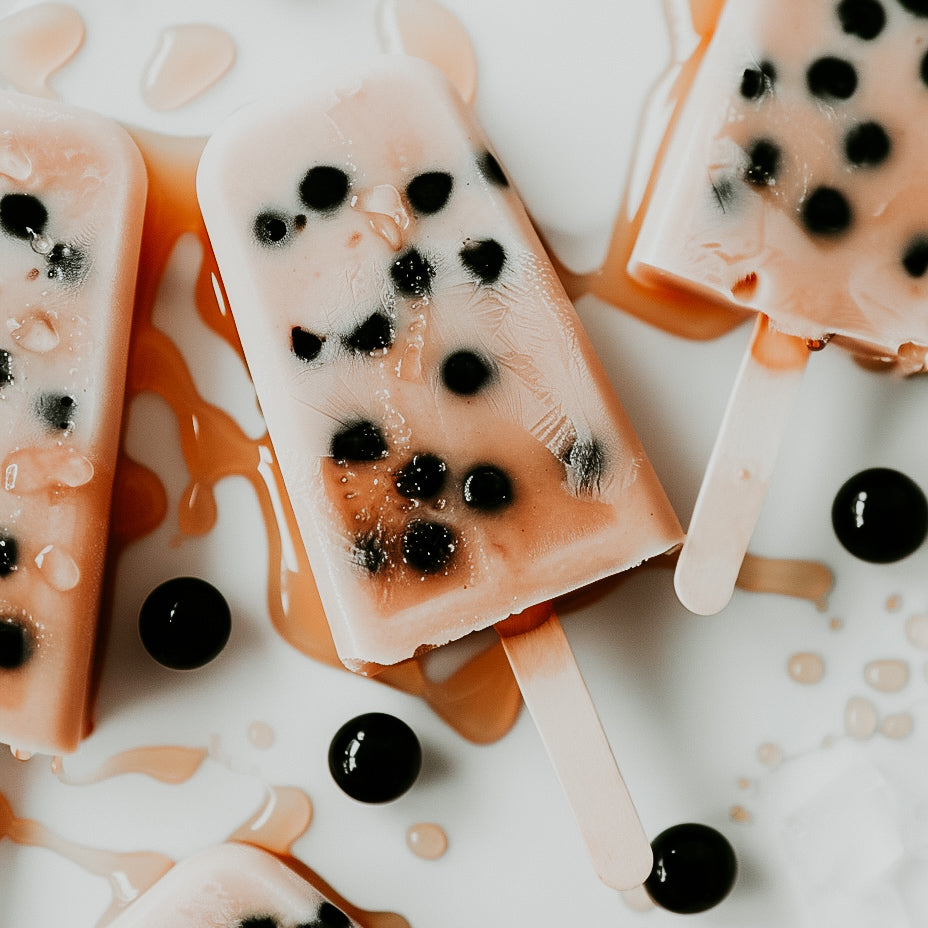 Popsicles with brown sugar ice cream texture, garnished with what appears to be honey boba, and drizzled with caramelized brown sugar syrup on a white surface.