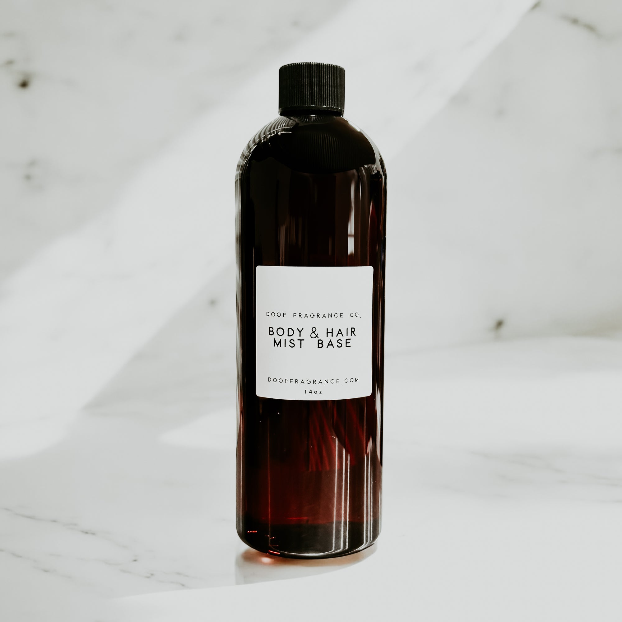 A clear bottle labeled 'BODY & HAIR MIST BASE' from Doop Fragrance Co., designed for containing custom body and hair fragrance mists.