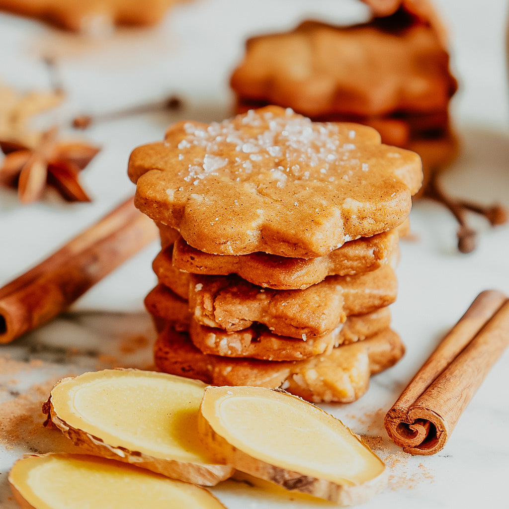 A stack of gingerbread cookies with cinnamon sticks and slices of ginger around them, suggesting a spicy fragrance oil.