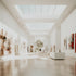 Interior view of a museum with natural lighting and multiple paintings displayed on the walls.