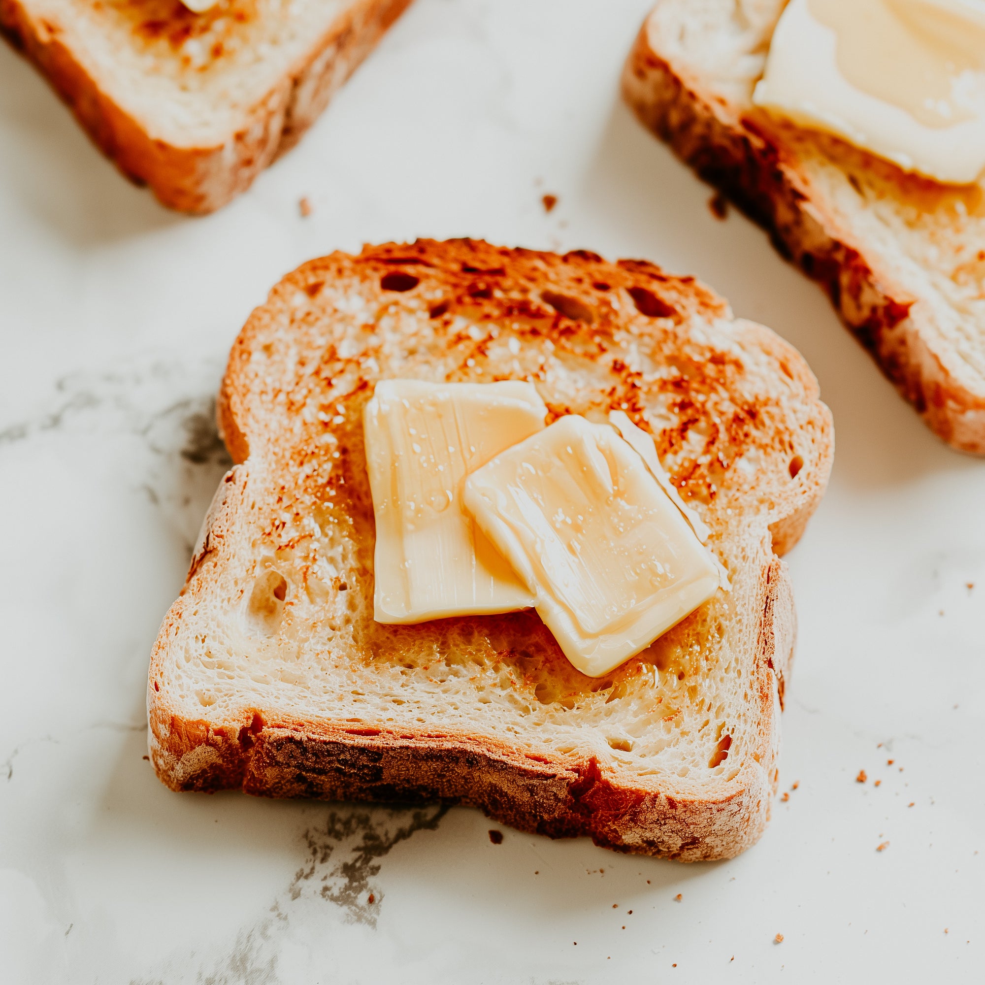 Slices of toasted bread with pieces of butter on top, placed on a marble surface.