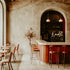 Interior of a cozy cafe with a bar counter, stools, and a few tables, with a soft focus on a fragrance oil bottle in the background.