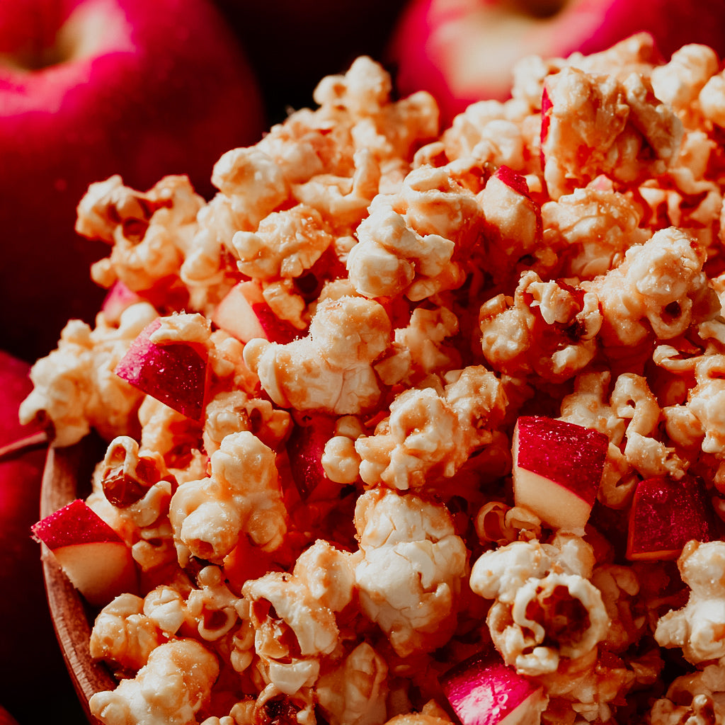 Close-up of caramel apple popcorn with red apple pieces in a wooden bowl.
