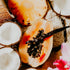 A photo of a halved papaya, a coconut cut open, and vanilla bean, arranged with a flower in the background.