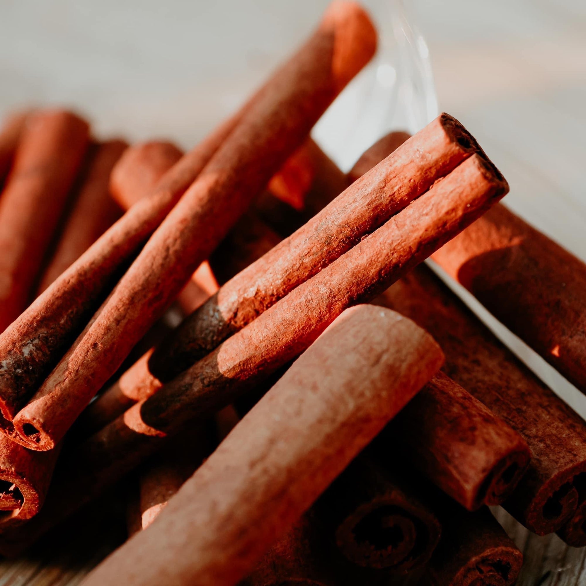 A close-up image of several cinnamon sticks arranged in a pile with a light source above them, casting a warm glow.