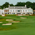 A well-manicured golf course with a country club house in the background, featuring large windows and a white exterior.