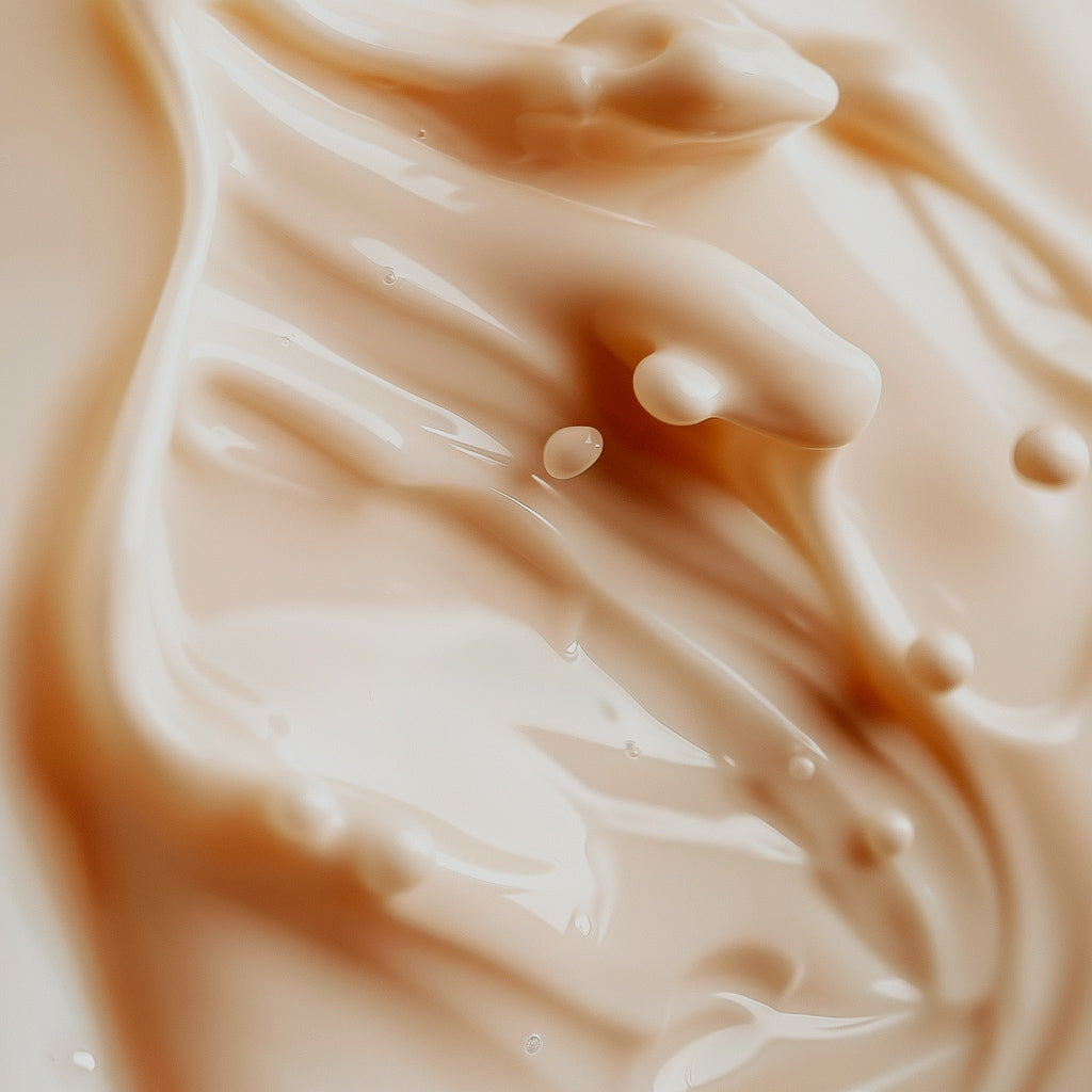 A close-up image of a creamy milk-colored fragrance oil with a smooth texture, showing droplets and ripples.