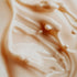 A close-up image of a creamy milk-colored fragrance oil with a smooth texture, showing droplets and ripples.