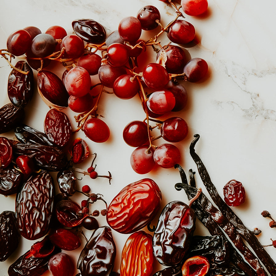 An assortment of dried fruits and fresh grapes, along with vanilla beans, arranged on a marble surface.