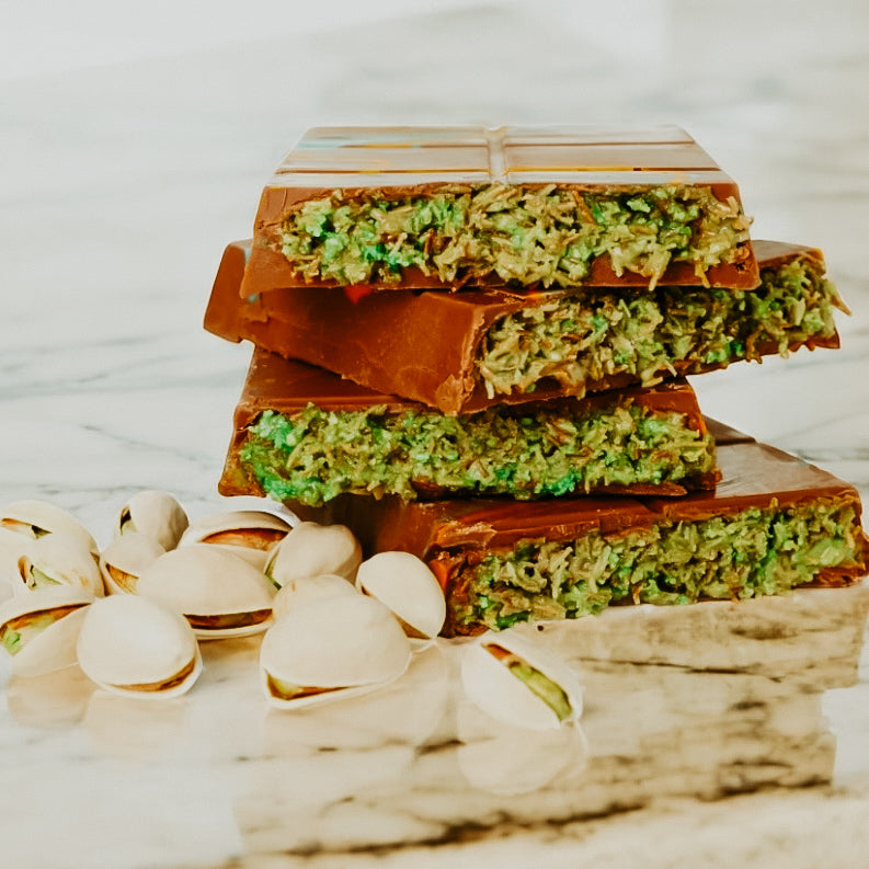 Stack of chocolate bars with green nougat on a marble surface with pistachios.