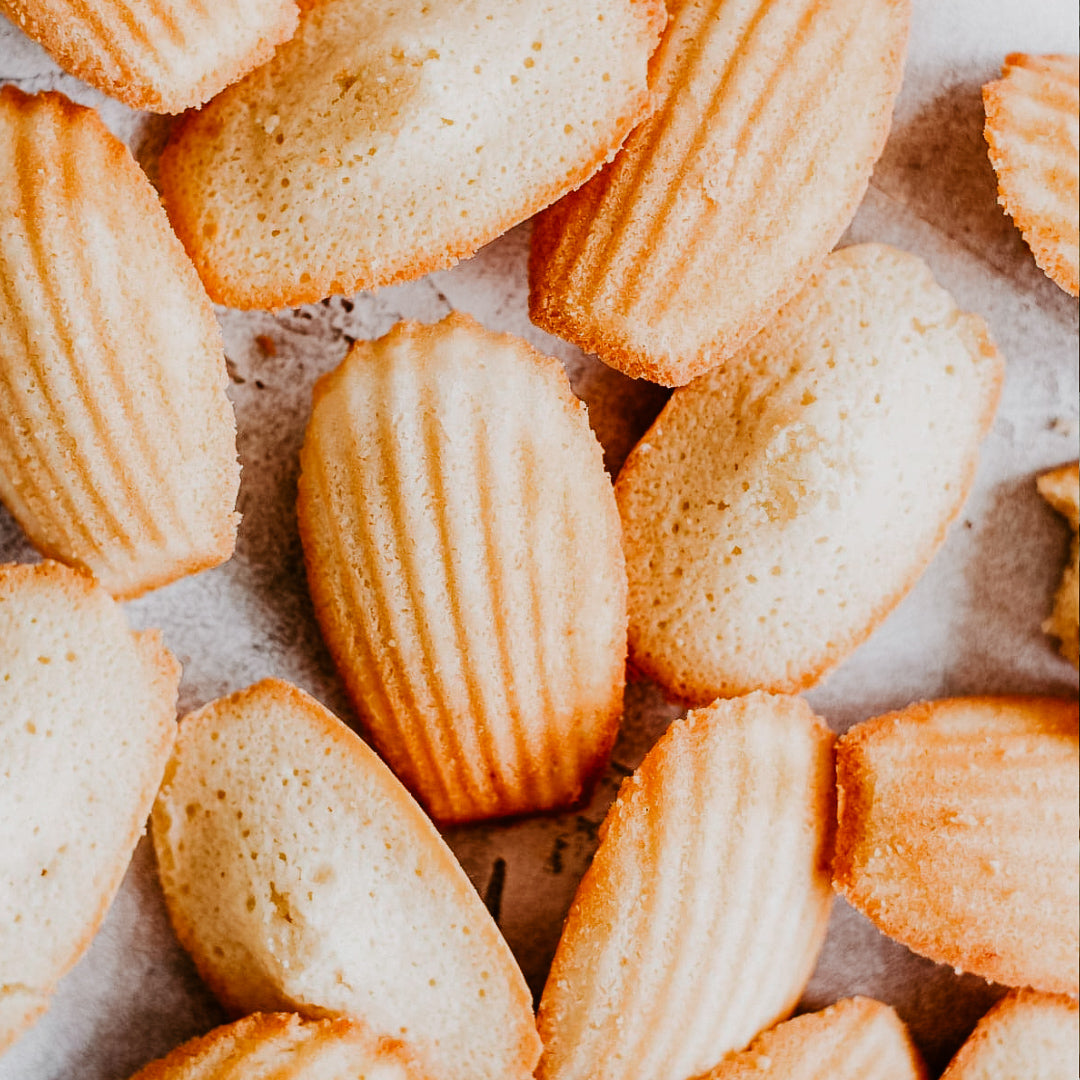 A close-up image of French Madeleines, which are small, sponge cakes with a distinctive ribbed texture and golden-brown edges.