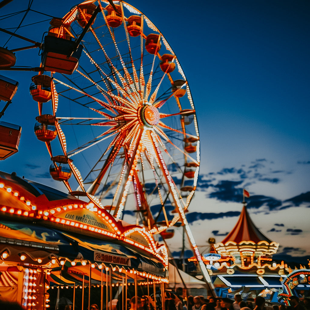A vibrant image of a funfair at dusk with a Ferris wheel and various fairground attractions lit up with bright lights.