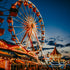 A vibrant image of a funfair at dusk with a Ferris wheel and various fairground attractions lit up with bright lights.