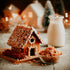 Gingerbread house with cinnamon sticks and a jar of milk on a wooden surface.