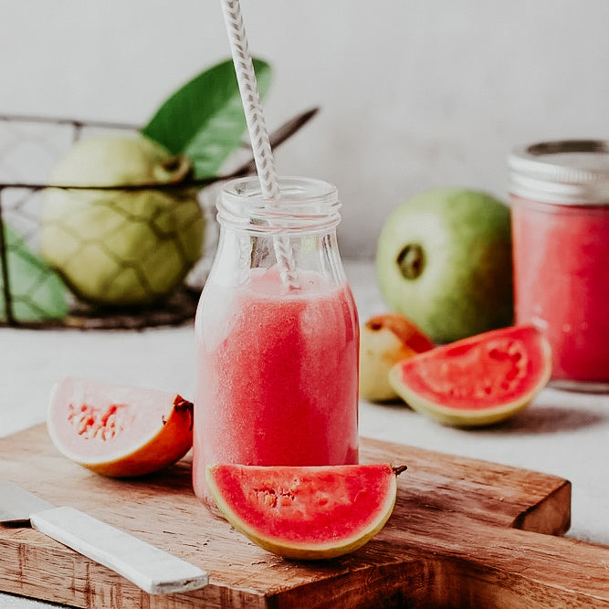 A bottle of Guava Nectar accompanied by slices of pink guava fruit and a whole guava in the background, placed on a wooden board.