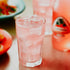 A glass of guava soda with ice, alongside a bottle of the fragrance oil and a plate of food in the background.