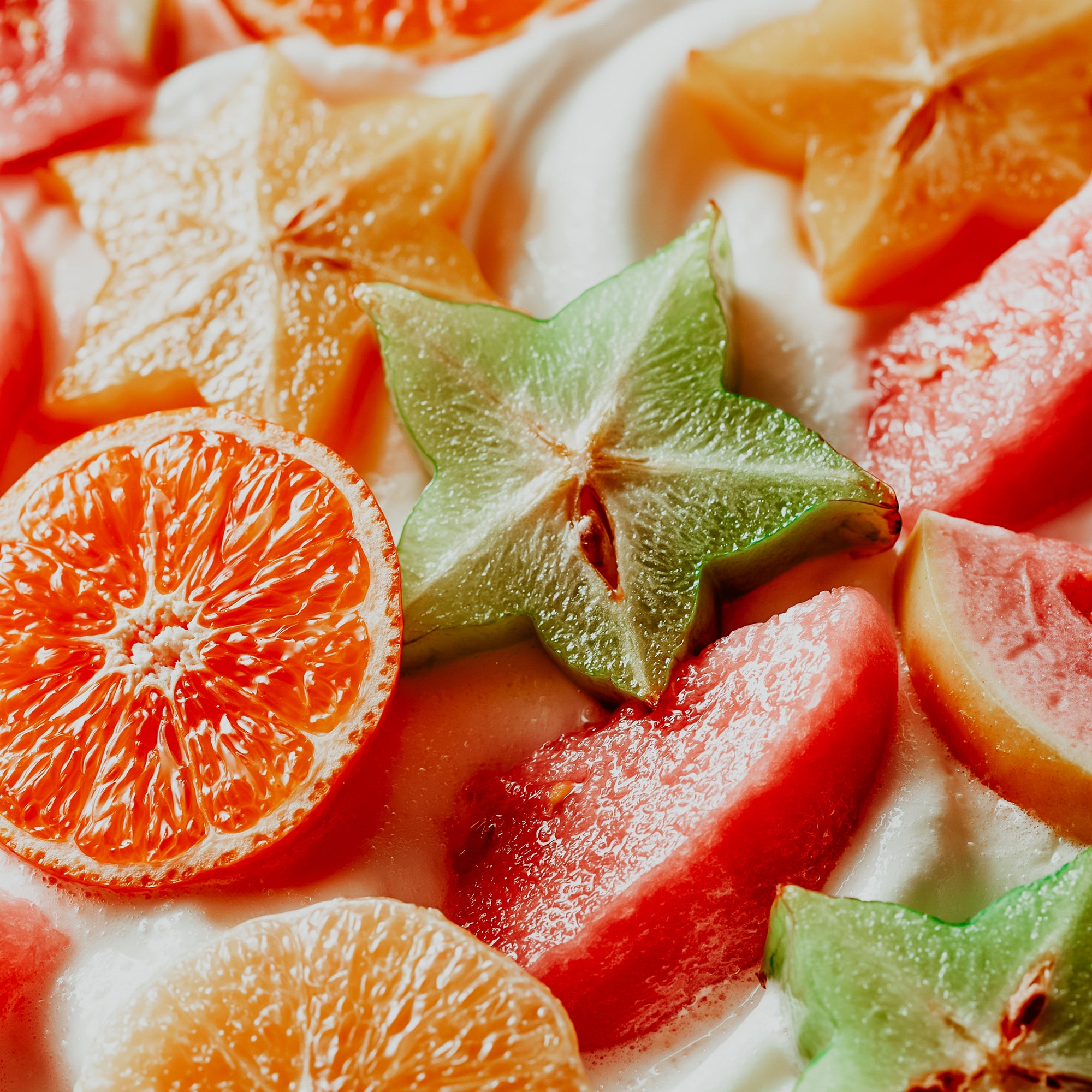 Close-up of sliced fruits including oranges, watermelon, and star fruit on a white background.