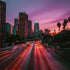 A cityscape at dusk with tall buildings and a pinkish-purple sky, featuring the movement of cars on a street.