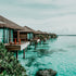 A scenic view of water villas in the Maldives with clear blue waters and a lush landscape.