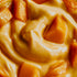Close-up of a creamy peach-colored dessert or spread with glossy chunks of orange fruit, likely mango or peach, filling the frame.