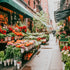A vibrant street scene featuring a flower market with various flowers displayed in front of shops, and people walking on the street.