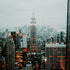 A cityscape with high-rise buildings, including the Empire State Building, during a rainy day, viewed from a high vantage point.
