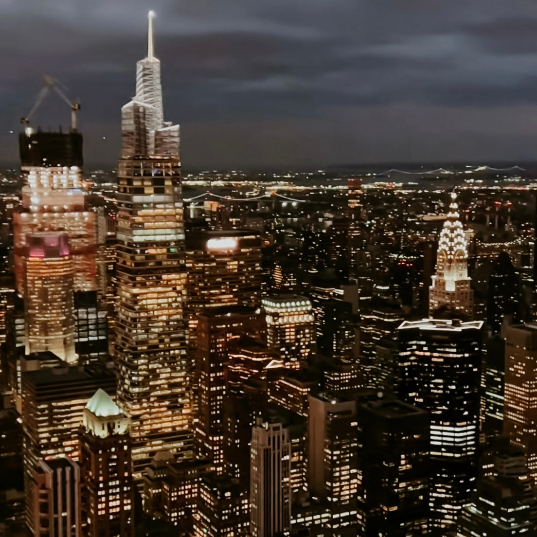 A nighttime cityscape of Manhattan with illuminated skyscrapers, including the Chrysler Building and the Empire State Building.