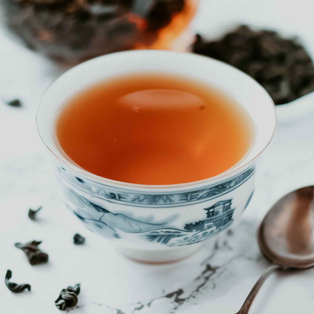 A cup of oolong tea with a tea bag visible in the background, on a white surface with a patterned design.