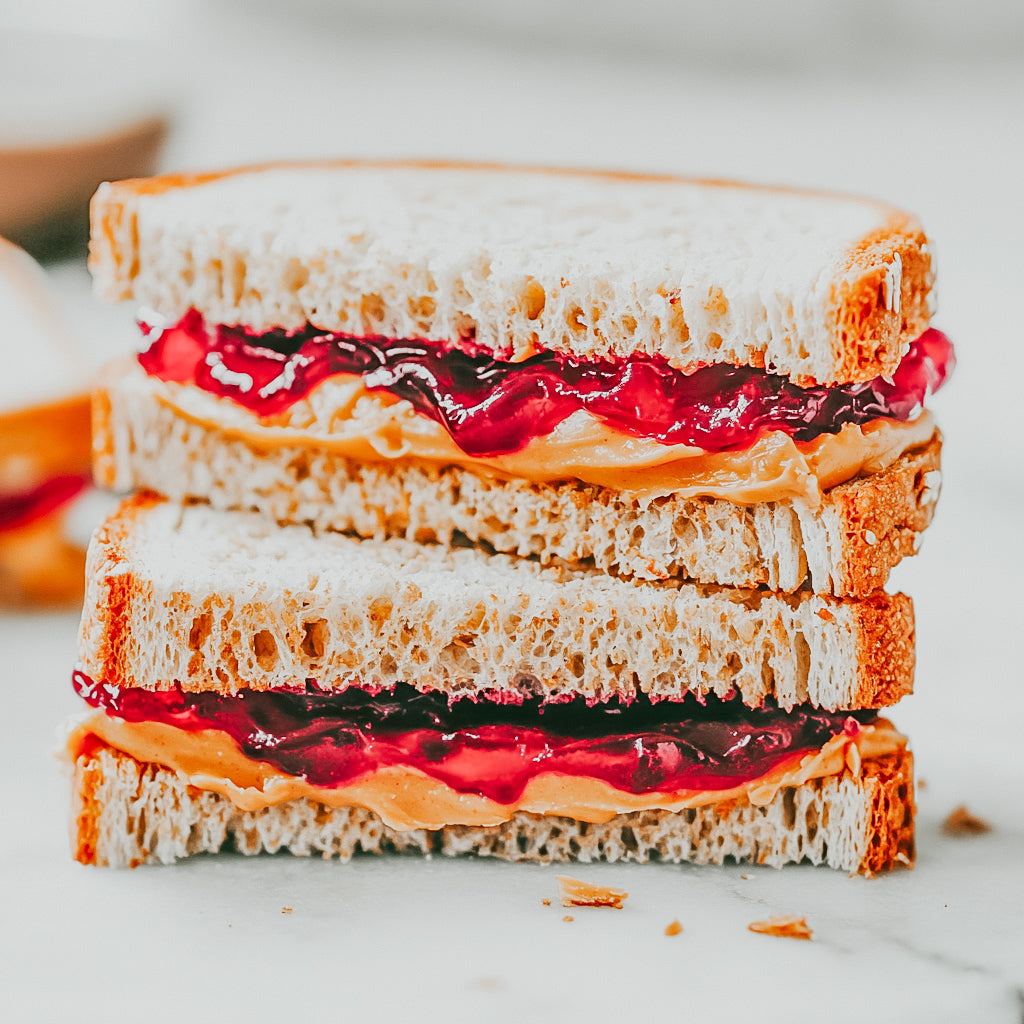 A sandwich with peanut butter and jelly spread between two slices of bread, placed on a white surface.