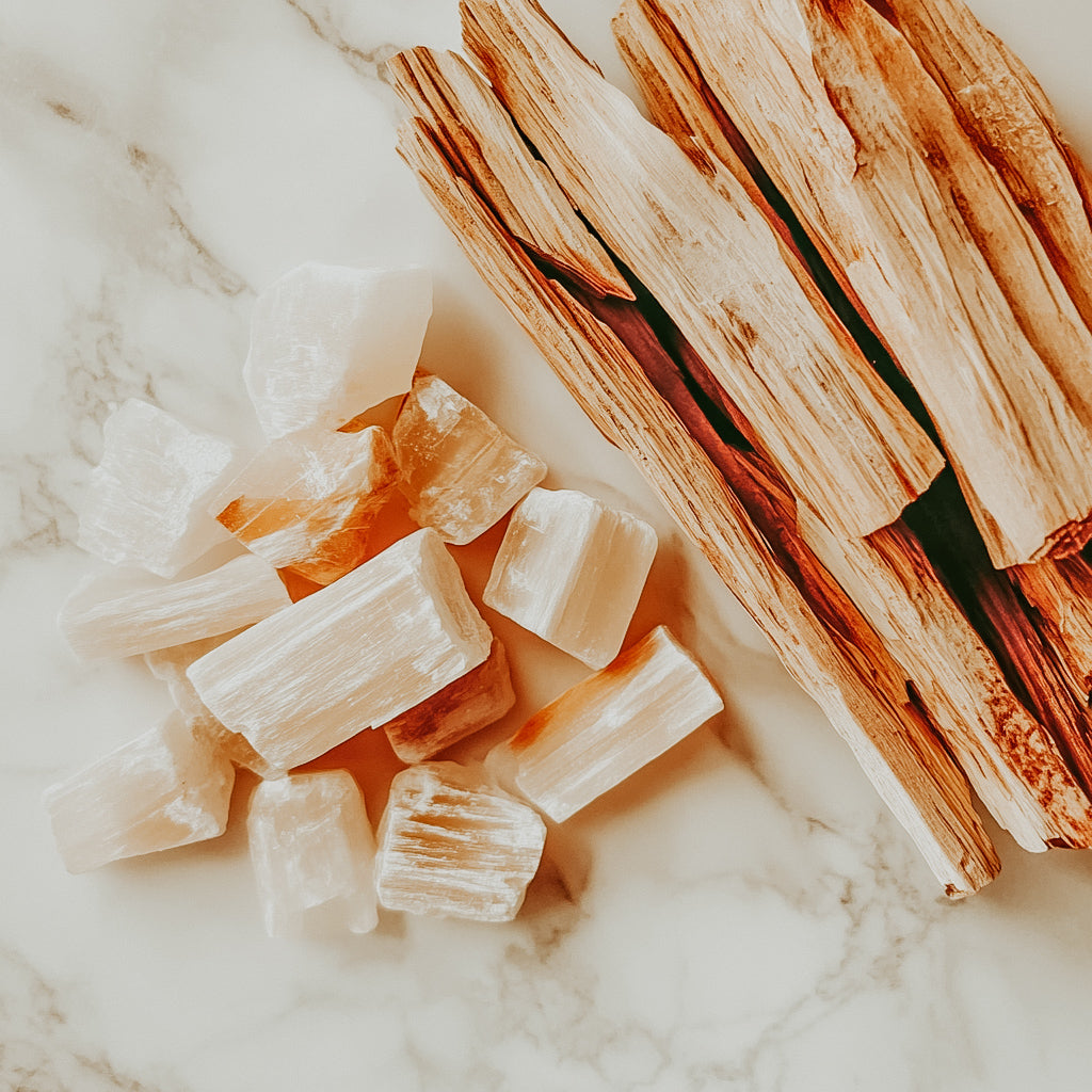 A collection of palo santo wood and white crystals on a marble surface.