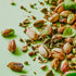 Scattered pistachio nuts and cardamom seeds on a green background