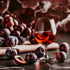 A glass of cognac surrounded by ripe plums, with a backdrop of marble and additional plums enhancing the luxurious feel of the image.
