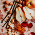 An assortment of food items including sliced pears, hazelnuts, vanilla pods, and petals arranged on a surface, possibly for scent or culinary purposes.