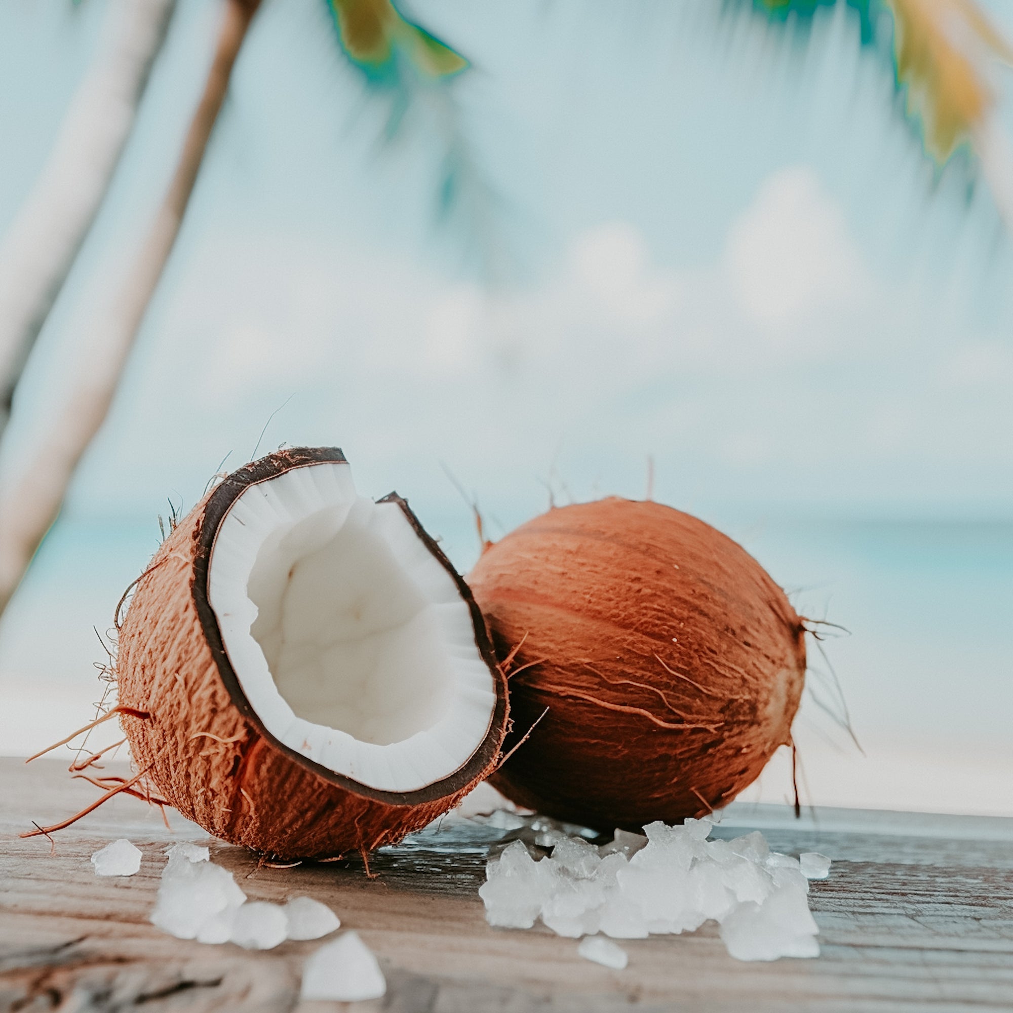 A image of a coconut and salt crystals on a wooden surface with a beach background.