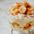 A bowl of Southern banana pudding with layers of bananas, vanilla custard, and whipped cream, topped with crushed wafers and a banana slice.