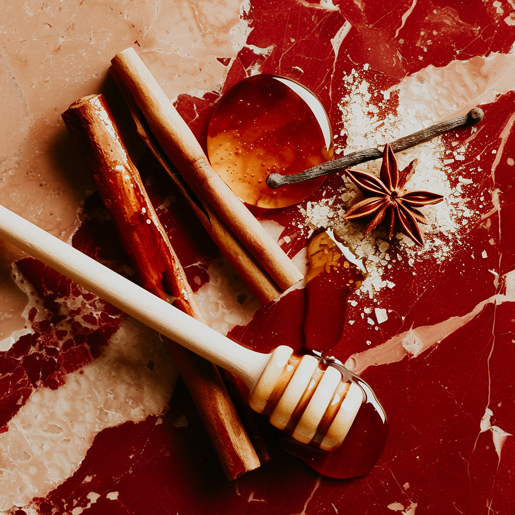 A composition of fragrance items including a honey dipper, cinnamon sticks, and anise star on a red textured background