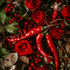 A close-up image of red roses, chili peppers, and other foliage, representing the 'Sriracha Rose' fragrance oil which combines spicy and floral notes.