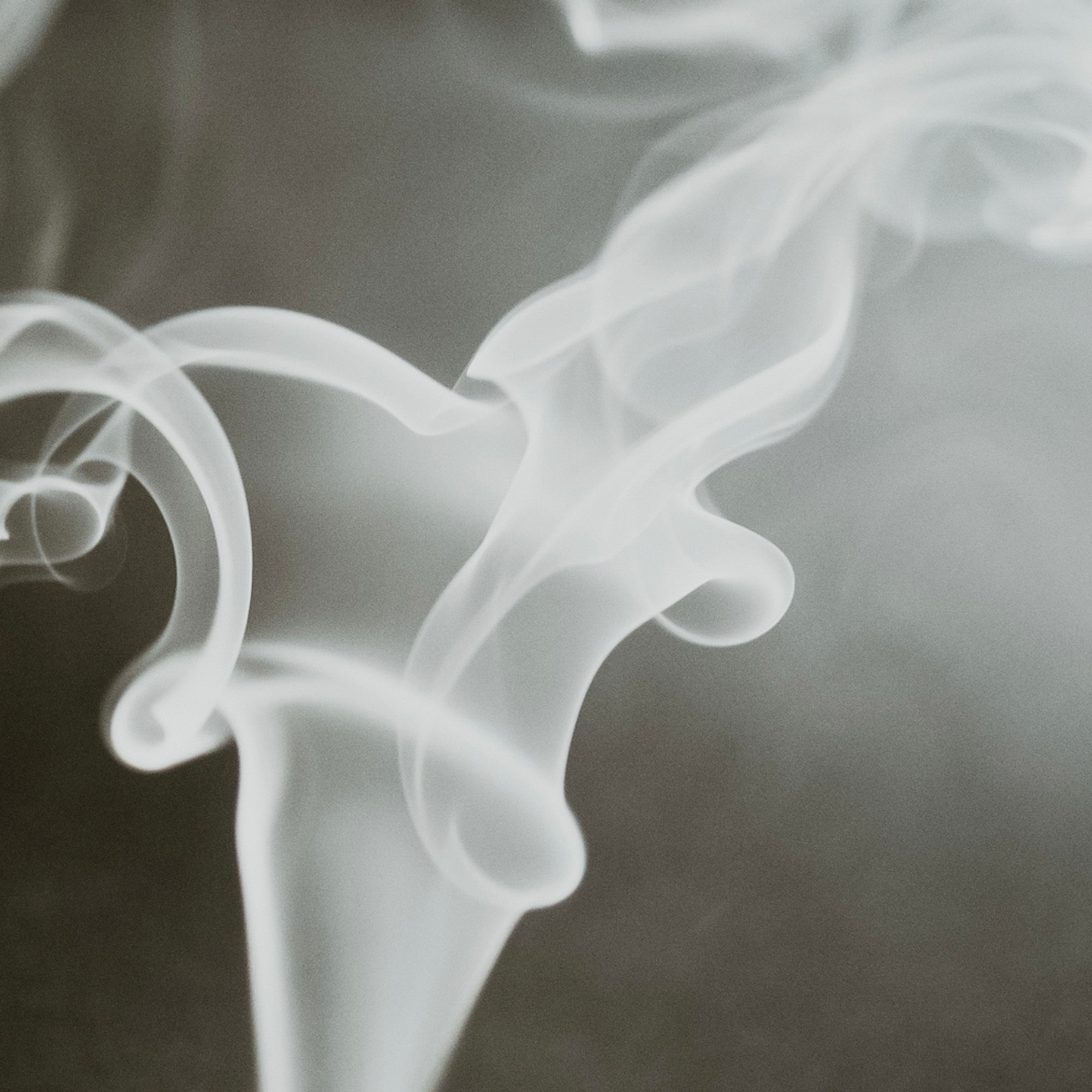 A photo of swirling white smoke against a dark background, reminiscent of smoke from a fire or incense.