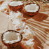 A fragrance oil bottle with an image of two coconuts and white flowers on a sandy surface, possibly suggesting the scent of coconut and floral notes in the product.