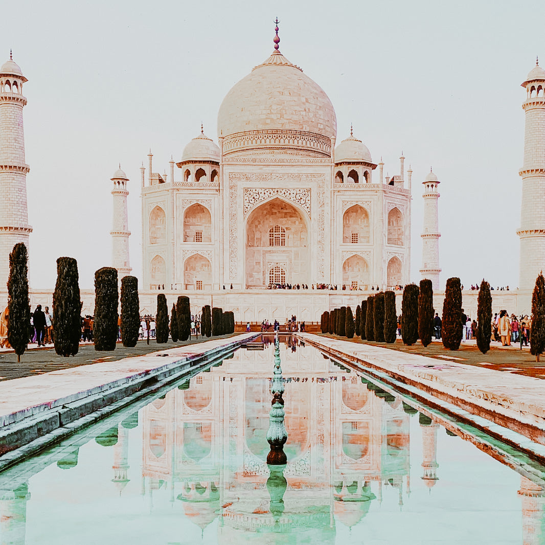 Image of the Taj Mahal reflecting in water, showcasing the iconic monument surrounded by greenery and a clear sky.
