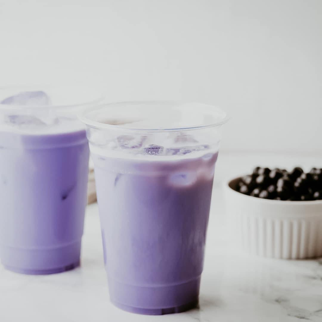 Two cups of purple-colored Taro Milk Tea with ice and a bowl of tapioca pearls in the background.