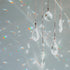 Transparent clear, teardrop-shaped crystals suspended on strings, with light reflecting off the bottles and creating rainbow-like patterns on a gray background.