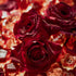 A close-up image of red roses with visible dew drops, surrounded by amber colored fragrance beads.