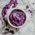 A small open container of ube jam spilled over the sides on a marble surface.