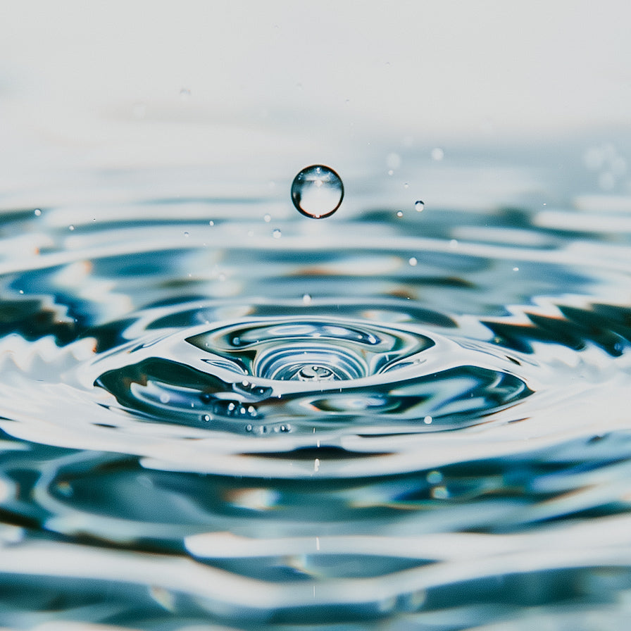 A close-up image of water droplets on a water surface creating ripples.