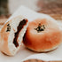 A photo of a red bean bun, showing the bread roll with a visible filling and black sesame seeds on top.