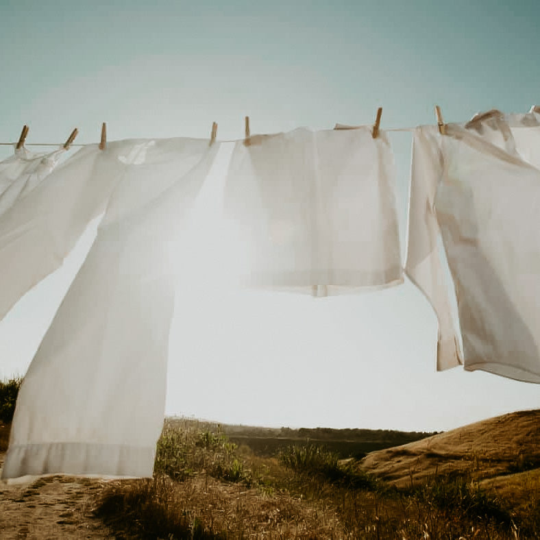 White linens drying on a clothesline outdoors with a landscape in the background.