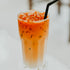 A glass of Thai tea with cream on top and a straw, representing the fragrance oil's connection to the scent of the beverage.